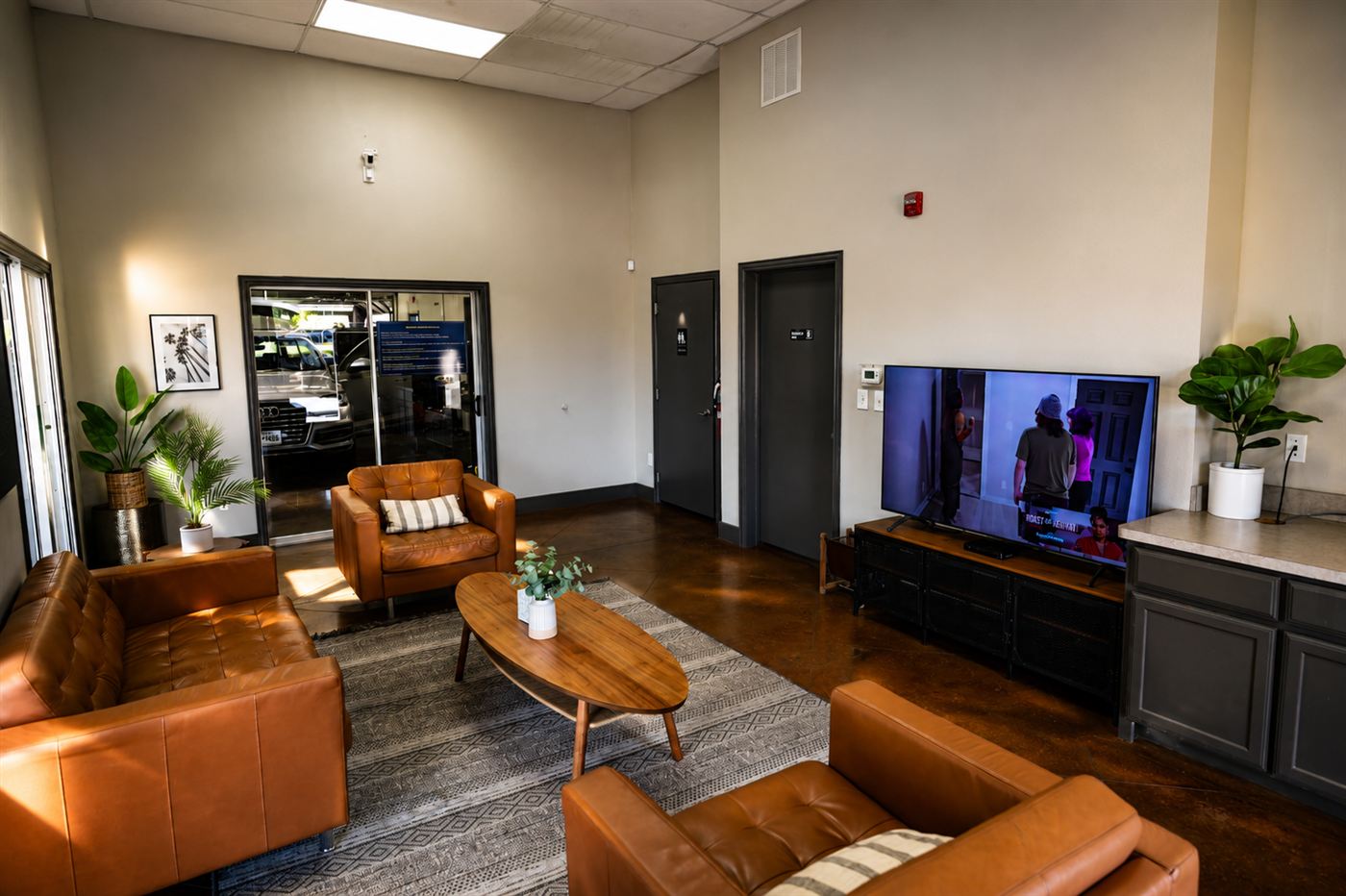 Quiet Detail Center lounge with tan leather chairs, a coffee table, plants, and a wall-mounted TV