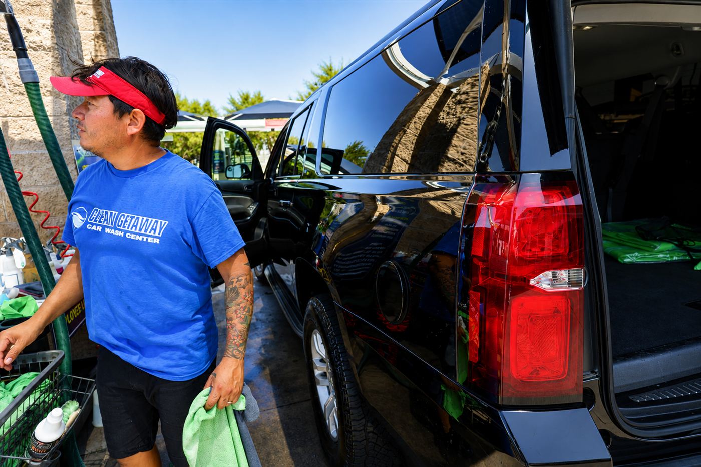 Crew member in a red visor towel-drying the side of a black SUV